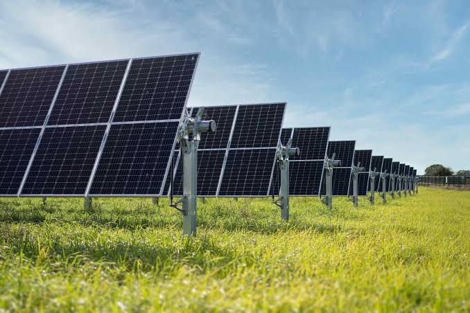 Solar farm with panels stretching across a green field under a bright blue sky